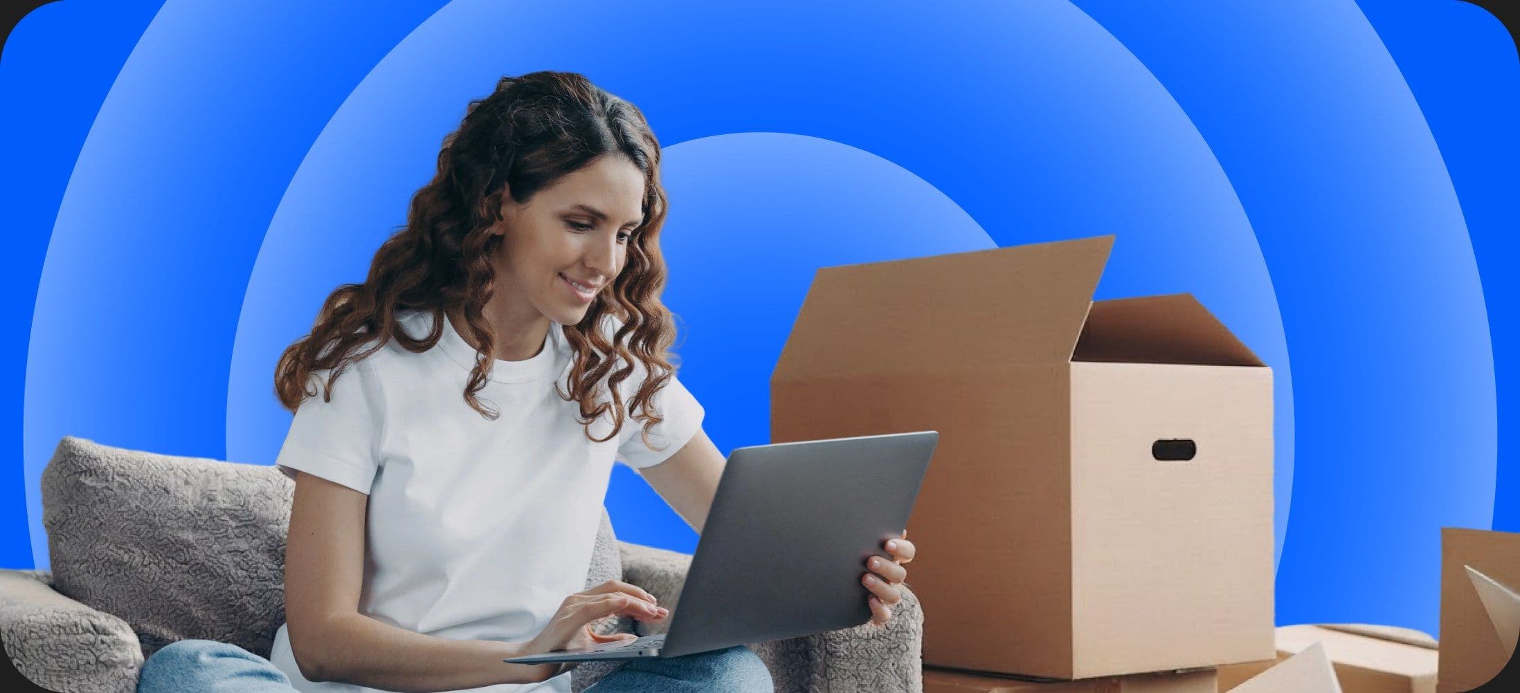 A woman sitting among moving boxes, using a laptop
